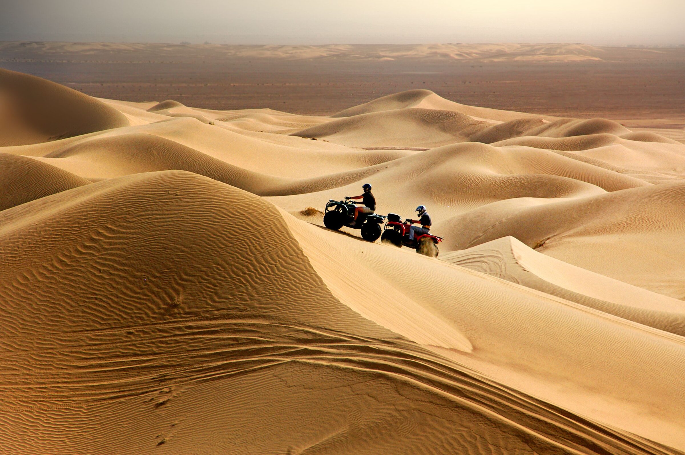 Two quad riders pausing on a high dune ridge in the Erg Chebbi desert near Merzouga